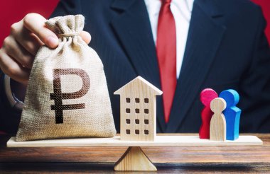 Adam Rus rublesi para çantasını ve evi aile terazisine koyuyor. İpotek, borç yükü. Konut yardımı, çocuk nüfusu artışını canlandırmak için genç ailelerin finansmanı. Çocuk Yardımı