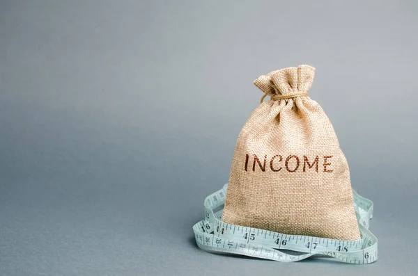 Money bag with the word Income and measuring tape. Reduced revenue and profits. Reduced budget. Loss of money. Unsuccessful business and poverty. Lower salary, wage rates. Financial crisis