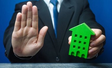 Man with a green house makes a stop gesture. Bank refusal to provide a mortgage loan. Housing problems, unscrupulous dishonest company builder. Confiscation pledged property. Refusal residence permit. clipart