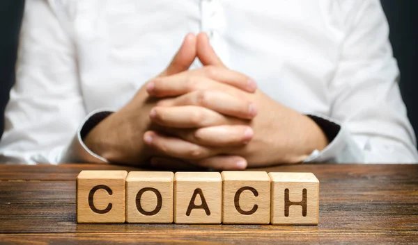 The inscription Coach and a man sitting with his hands clasped in a lock. Trainer and mentor. Self improvement. Achieving goals through training and guidance. Skills development