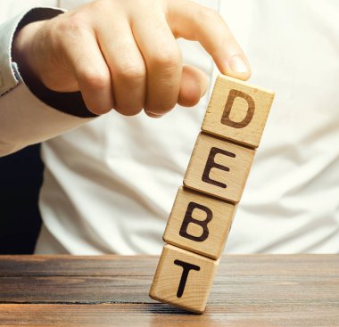 İşadamı ahşap blokları borçla kaldırır. Borç azaltma veya iptali, borçların kısmi veya topyekûn affedilmesi veya büyümenin yavaşlatılması veya durdurulmasıdır. Yeniden yapılanma. Öde. Kefaret