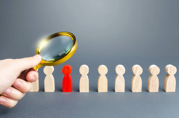 A hand with a magnifying glass studies a red person in a row of people. Identification, examination and isolation of potential carrier hostels of dangerous infections and diseases to prevent spread