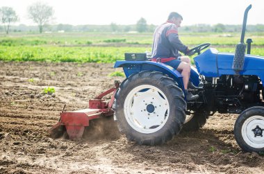A farmer on a tractor cultivates a farm field. Soil milling, crumbling and mixing. Agriculture, growing organic food vegetables. Loosening the surface, cultivating the land for further planting. clipart