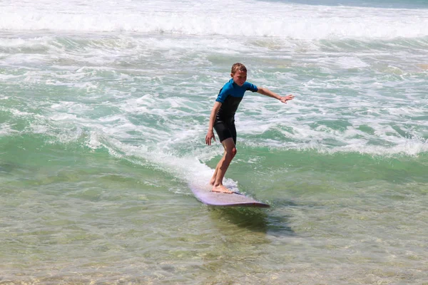 ビーチで紫色のロングボードに乗って波に乗る少年. — ストック写真