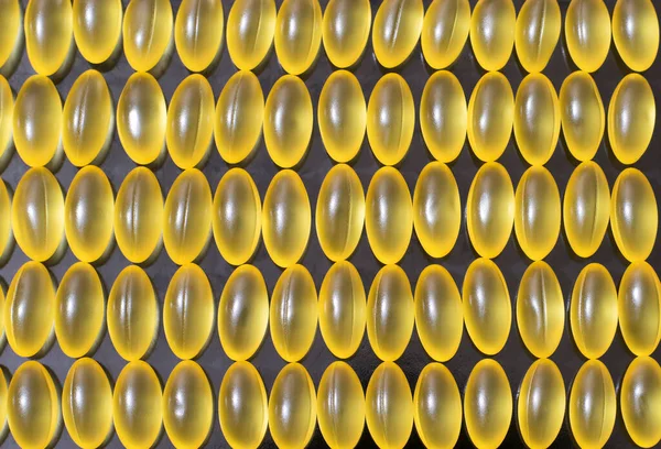 Куча желтых прозрачных капсул витаминов на черном фоне — стоковое фото