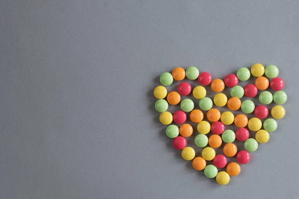 Hjärtform från flerfärgade tabletter av drakar på en grå vävd bakgrund — Stockfoto