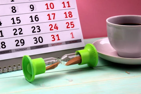 hourglass stand on the background of a calendar and a cup of coffee
