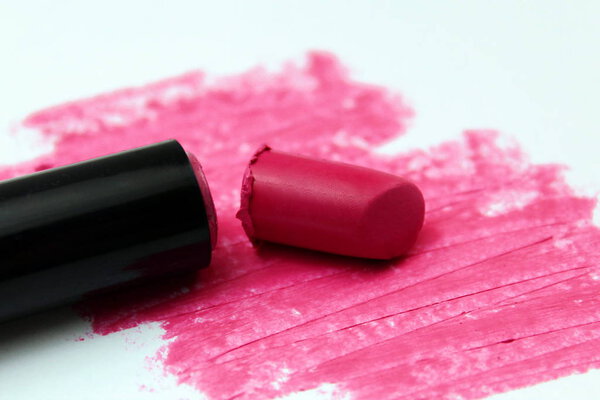 Broken bright pink lipstick lies on a white background