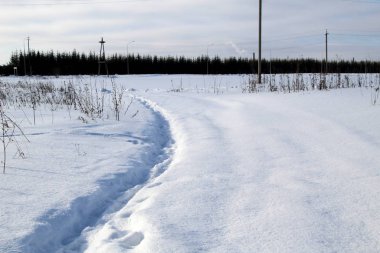 Güneşli bir günde kar yığınları arasında kış yolu