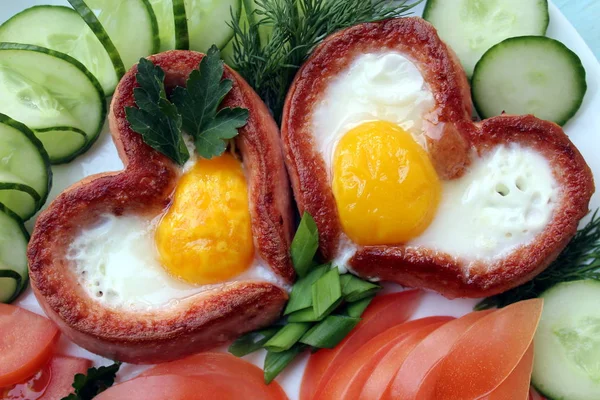 Beyaz bir tabakta yumurta ve sebzeli sosis kalbi var.