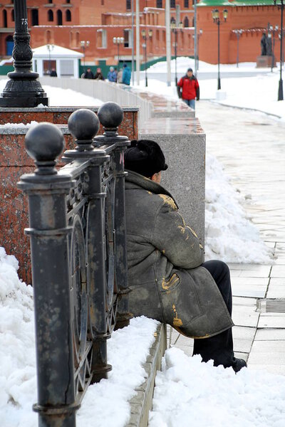 A man sits in winter in old clothes with a floor