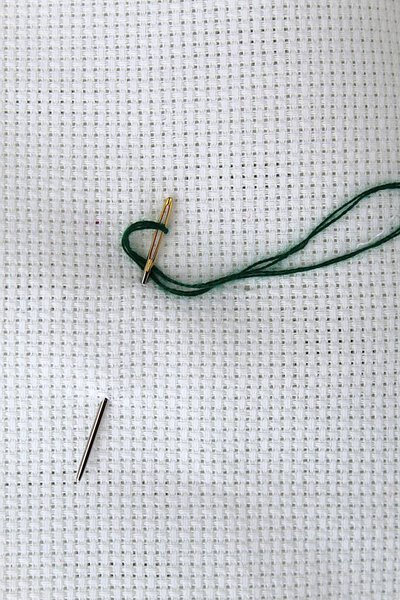 A needle with a green thread for embroidery attached to the fabric
