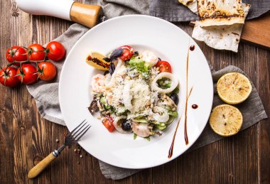 Koyu ahşap arka plan üzerinde beyaz bir plaka üzerinde deniz ürünleri salatası 