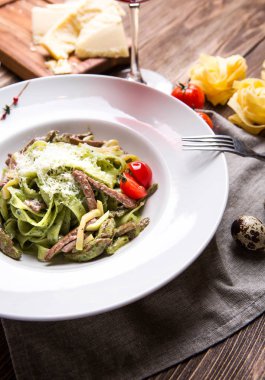 Karanlık wo beyaz bir tabağa et ve parmesan ile yeşil makarna