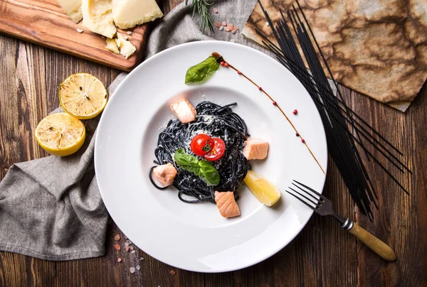 Pasta with cuttlefish ink, salmon and cherry tomatoes in a white