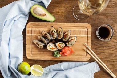 Wasabi, zencefil soya sosu ve chopsticks ve bir kadeh şarap ile Japon suşi rulo bir ahşap tahta üzerinde