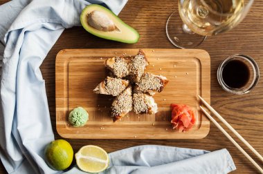 Wasabi, zencefil soya sosu ve chopsticks ve bir kadeh şarap ile Japon suşi rulo bir ahşap tahta üzerinde