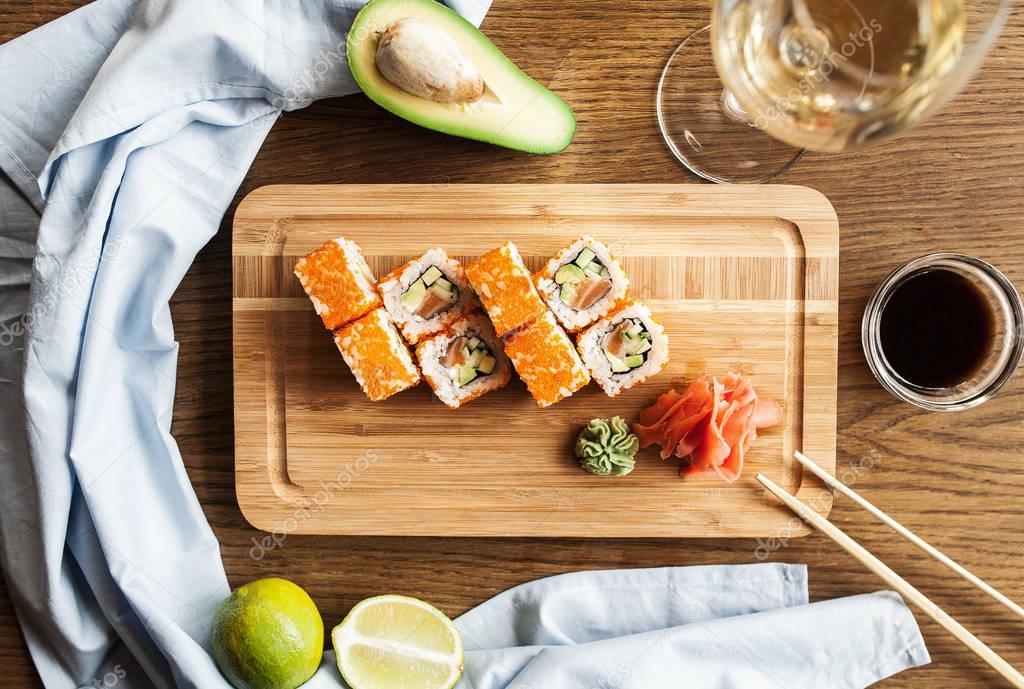 Japanese sushi rolls with wasabi, ginger soy sauce and chopsticks and a glass of wine on a wooden board