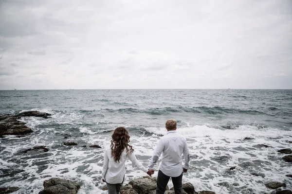 stylish couple in jeans and shirts on the background of the cold autumn sea in the gloomy weather