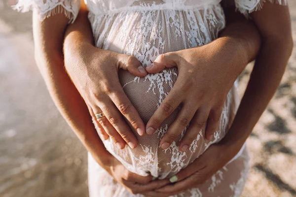 women's and men's tanned hands on a pregnant belly