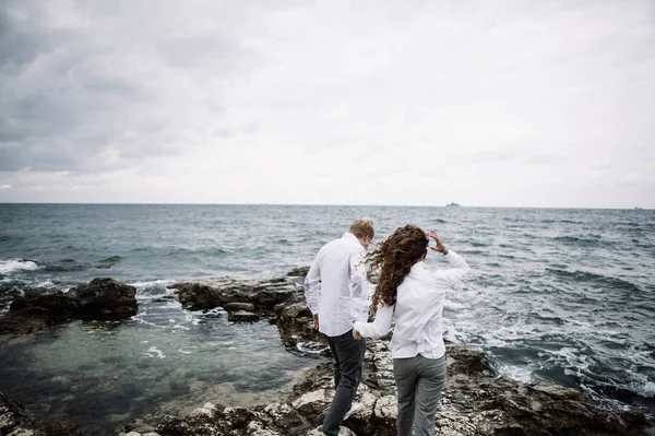 stylish couple in jeans and shirts on the background of the cold autumn sea in the gloomy weather