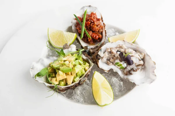 restaurant luxury appetizer of oysters, avocado and sun-dried tomatoes on a plate with ice