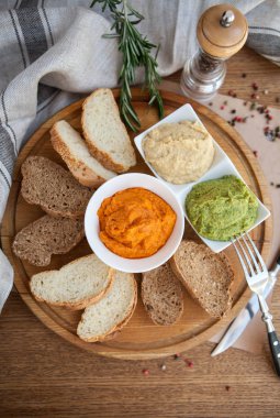 Humus üç farklı tür: Humus, ıspanak, humus kırmızı biber ve klasik humus ekmek ile ahşap bir tahta üzerine dilimlenmiş