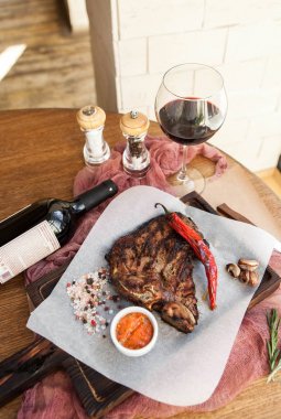 Acılı ve baharatlı sos bir kadeh kırmızı şarap ile ahşap bir gemide t-Bone biftek ızgara