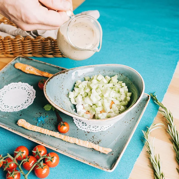 Summer soup okroshka with tiger shrimp and fresh cucumber in a blue plate, and the hand is pouring from above — Stock Image Summer Soup Okroshka Tiger Shrimp Fresh Cucumber Blue Plate Hand Stock Image