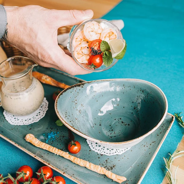 Summer soup okroshka with tiger shrimp and fresh cucumber in a blue plate, and the hand pouring ingredients — Stock Image Summer Soup Okroshka Tiger Shrimp Fresh Cucumber Blue Plate Hand Stock Picture