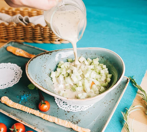 Summer soup okroshka with tiger shrimp and fresh cucumber in a blue plate, and the hand is pouring from above — Stock Image Summer Soup Okroshka Tiger Shrimp Fresh Cucumber Blue Plate Hand Stock Image