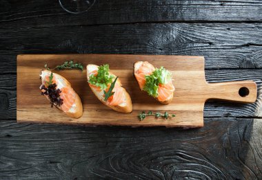 Üç bruschettes peynir ve bir ahşap tahta üzerinde taze somon ile 