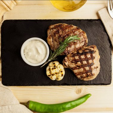 Kızarmış madalyonlar, sarımsak, biber ve biberiye taş oyun tahtası beyaz sos ile