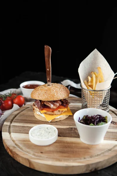 Burger with wheat loaf, French fries and salad on a wooden board