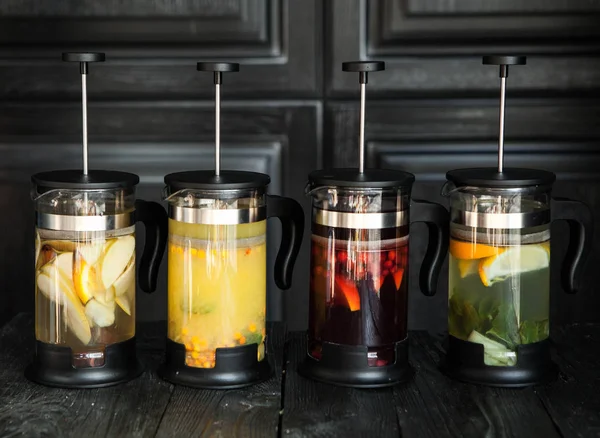 four french presses with different teas on a wooden background