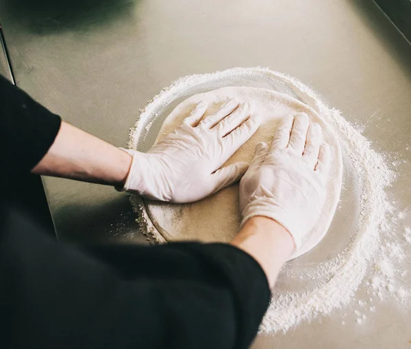 Hands of the man knead the dough on the flour on the kitchen surface