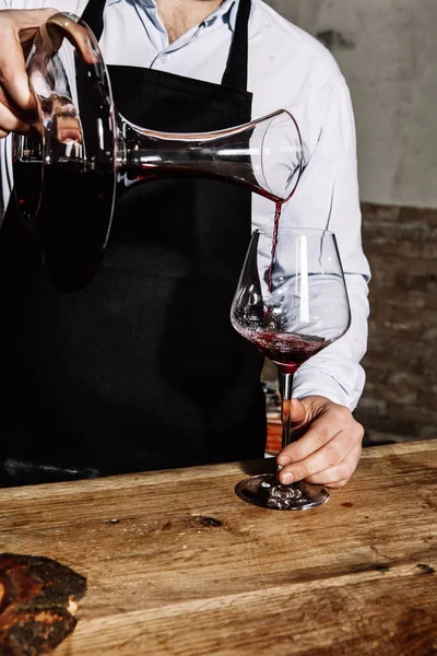 ブラック エプロンと光のシャツでソムリエがガラスにデカンタから赤ワインを注ぐ — ストック写真