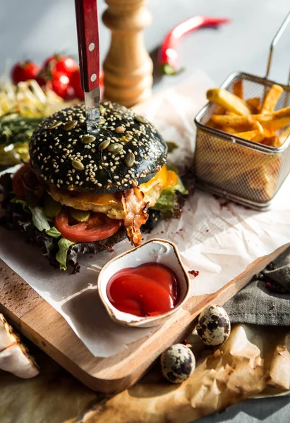 fast food, black burger with French fries and sauce on a wooden board