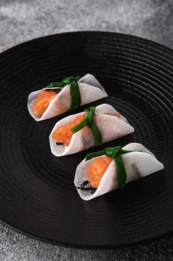 Atıştırmalıklar, amusebouche, aperatifler, parmak yiyecekleri siyah tabakta daikon dilimli krema soslu somon balığı.