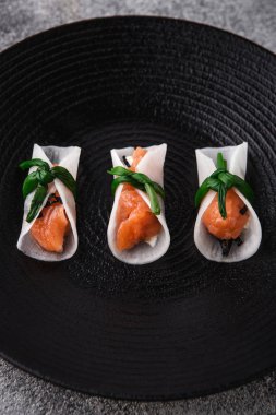 Atıştırmalıklar, amusebouche, aperatifler, parmak yiyecekleri siyah tabakta daikon dilimli krema soslu somon balığı.