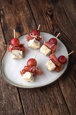 Atıştırmalıklar, amusebouche, aperatifler, parmak yiyecekleri - mavi cheeze, jamon, ahşap arka planda üzümler