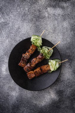 Atıştırmalıklar, amusebouche, aperatifler, parmak yiyecekler - Mini domuz göbeği, siyah tabakta salatalık dilimli domuz şişleri