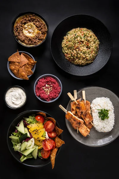 Όμορφα σερβίρεται τραπέζι με ποικιλία μεσογειακών πιάτων: χούμους, σαλάτα, tabule, ρύζι, κοτόπουλο σουβλάκια, νάτσος σε μαύρο φόντο flatlay Φωτογραφία Αρχείου