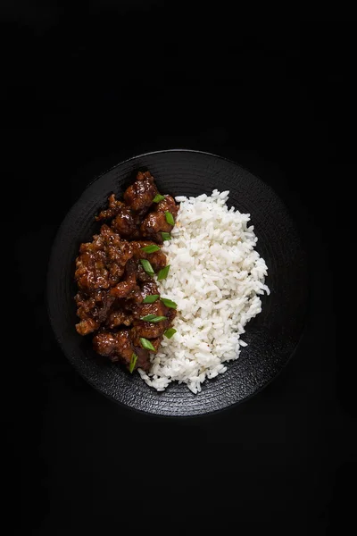Asian lunch rice with teriyaki chicken with green onion on black plate on black background