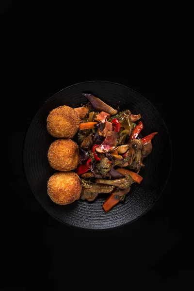 Ψητά ασιατικά λαχανικά με τρεις κροκέτες κοτόπουλου σε μαύρο πιάτο και σε μαύρο φόντο Εικόνα Αρχείου