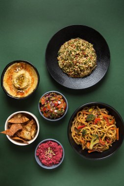 Çeşitli Ortadoğu usulü yemekler klasik humus, pembe humus, tortilla, tabul yeşil arka planda sebzeli erişte.