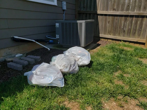 Pile of filty trash bags in back yard of residential home.