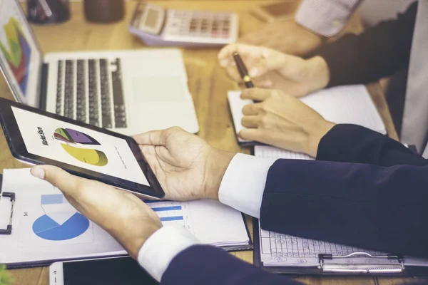 Close-up shots of the hands of a group of businessmen are meeting within the meeting room. Story market share trends. Have the graph displayed on the screen and Tablet laptops.