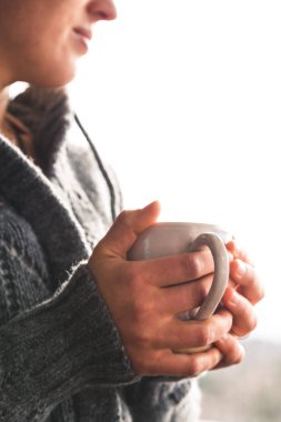 Fincan çay giyen gri yünlü hırka bir pencereden dışarı bakıyor tutan kadın