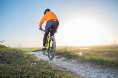 Turuncu bir kapüşonlu bir bisikletçi dağ yolu boyunca bisiklet sürmek. Doğa sporları kavramı. Dağlarda eğitim.